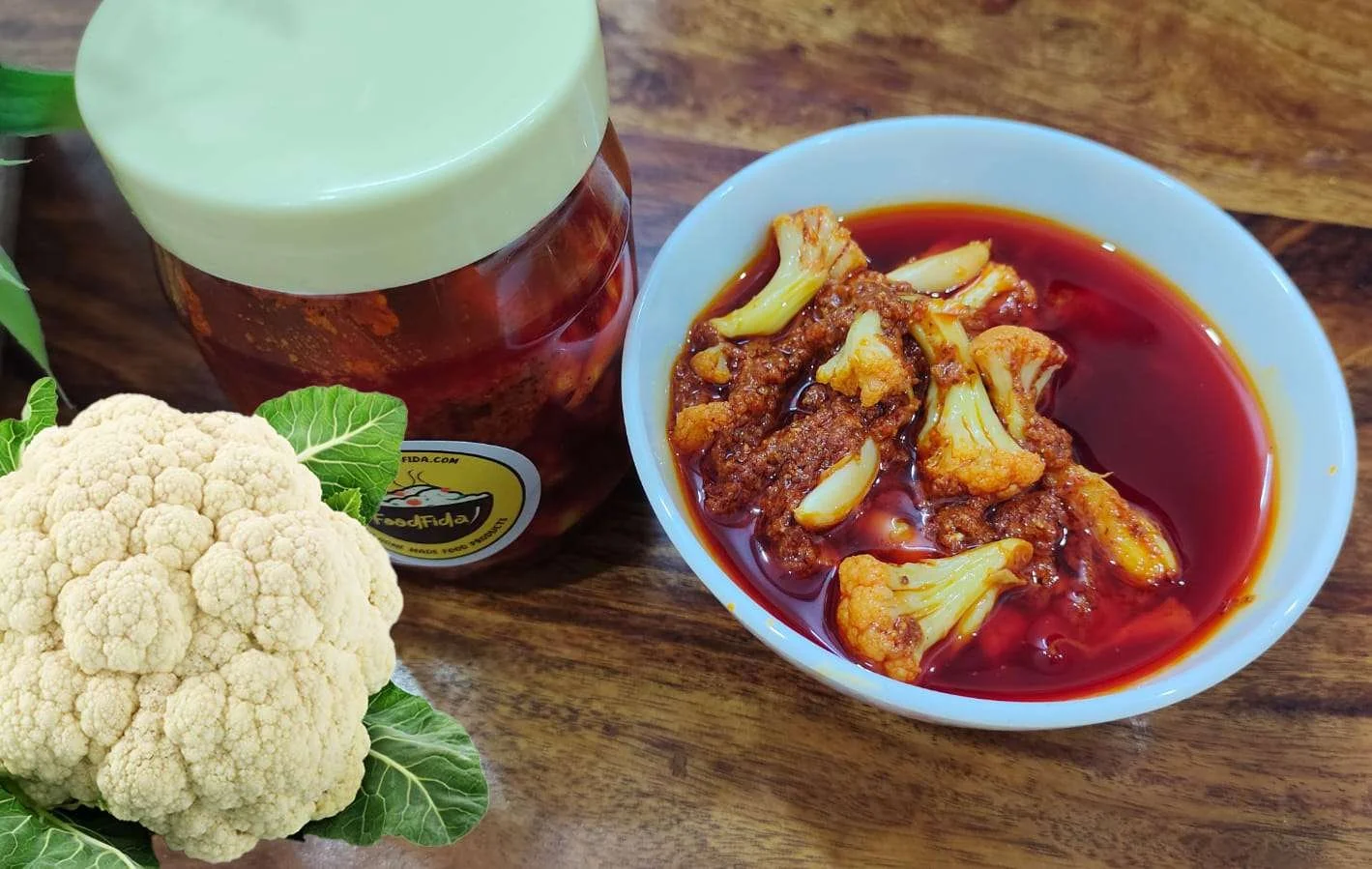 Homemade cauliflower pickle with traditional Indian spices, served in a glass jar with fresh cauliflower florets and red chilies.